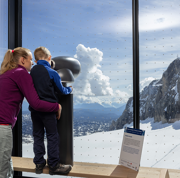 Person mit Kind nutzt ein digitales Fernrohr mit Blick auf den Hallstätter Gletscher.